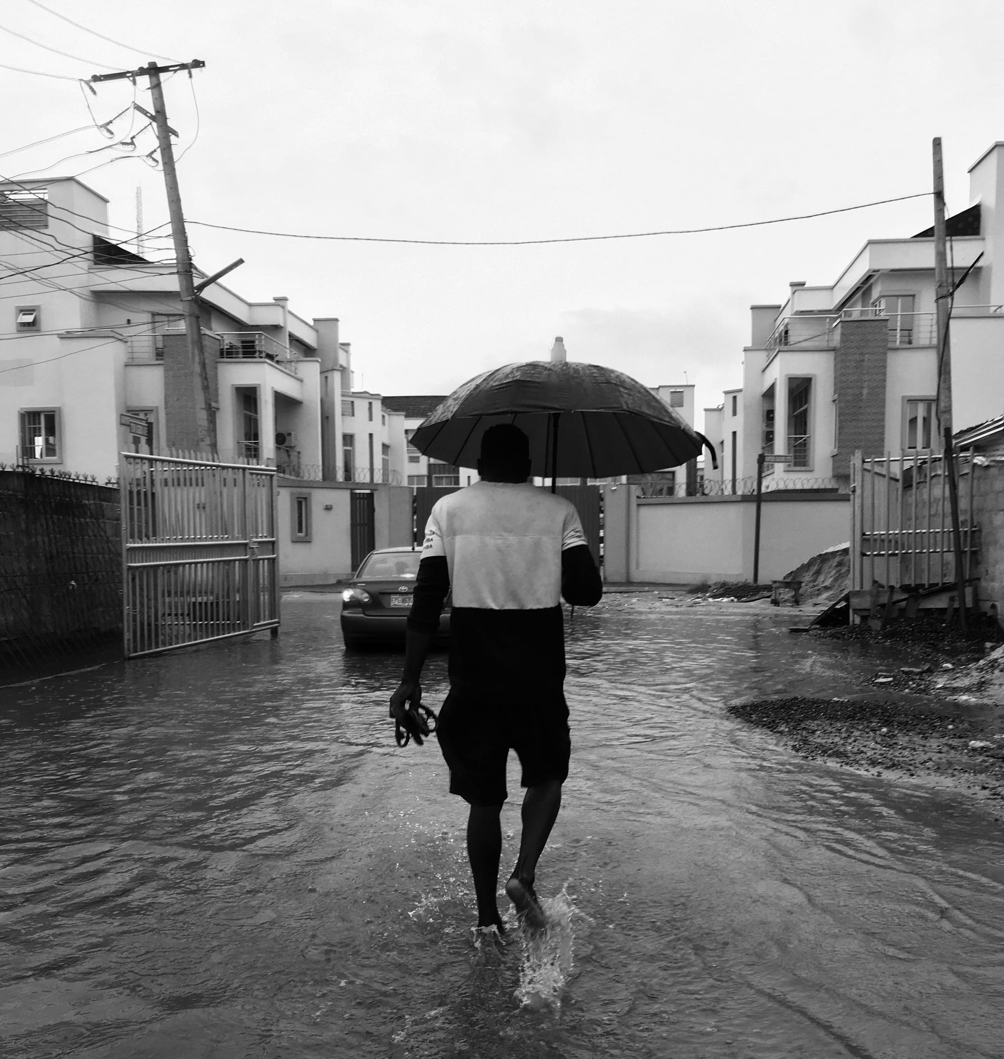 grayscale photo of woman in white long sleeve shirt and black pants holding umbrella walking on on on on on